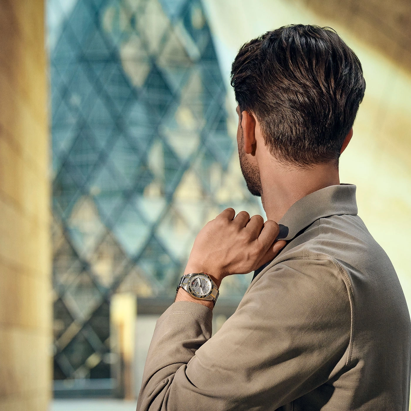 Man wearing a watch, looking at a modern building, appearing thoughtful.