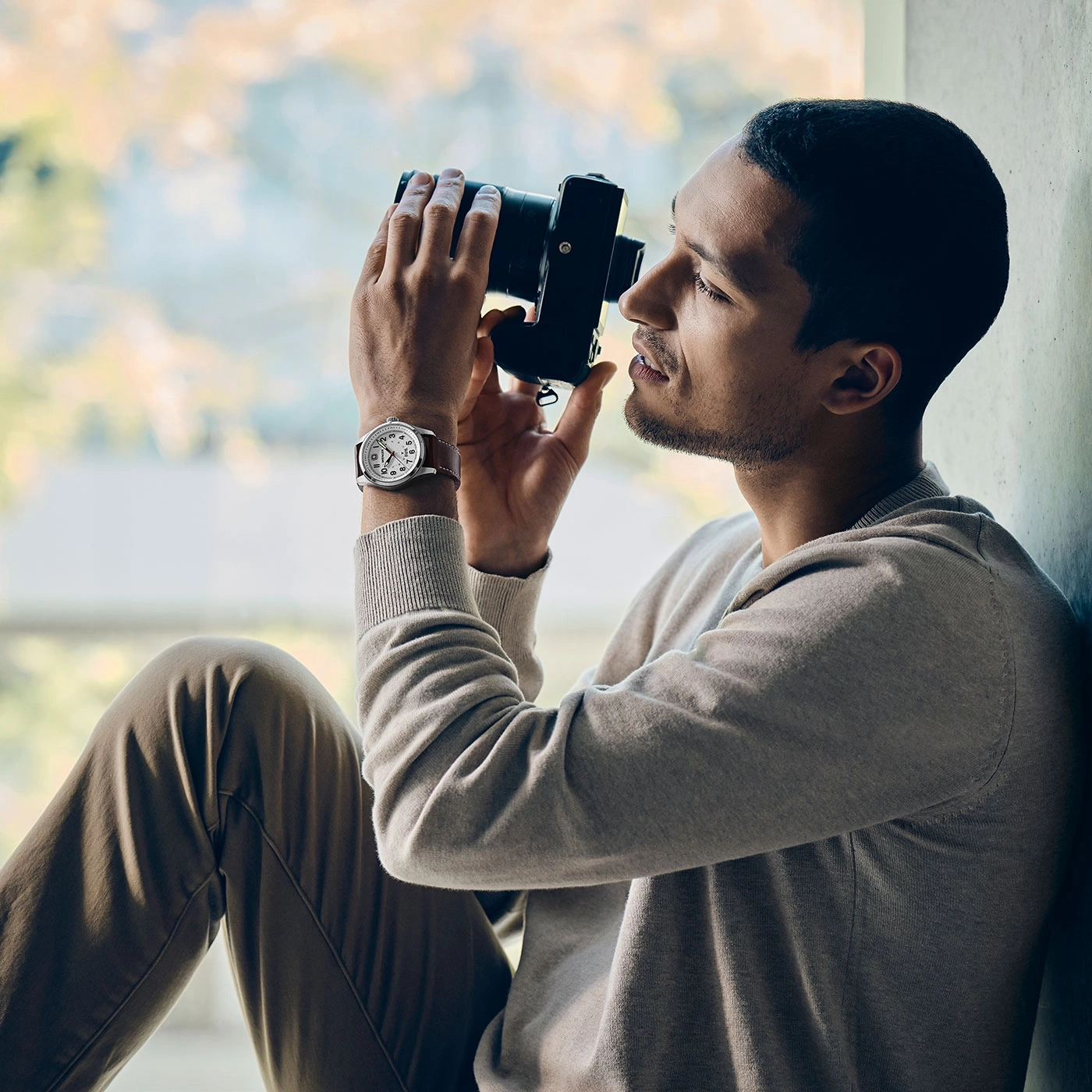 A man sits and photographs with a camera, wearing a watch.