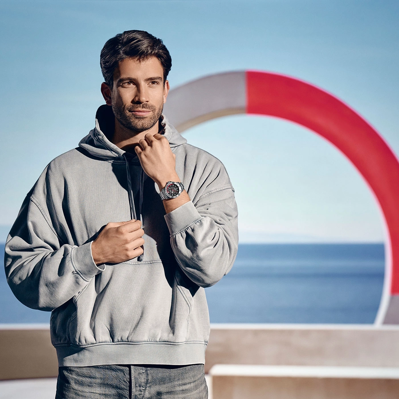Mann mit Uhr und Kapuzenpullover vor Meer und Rettungsring