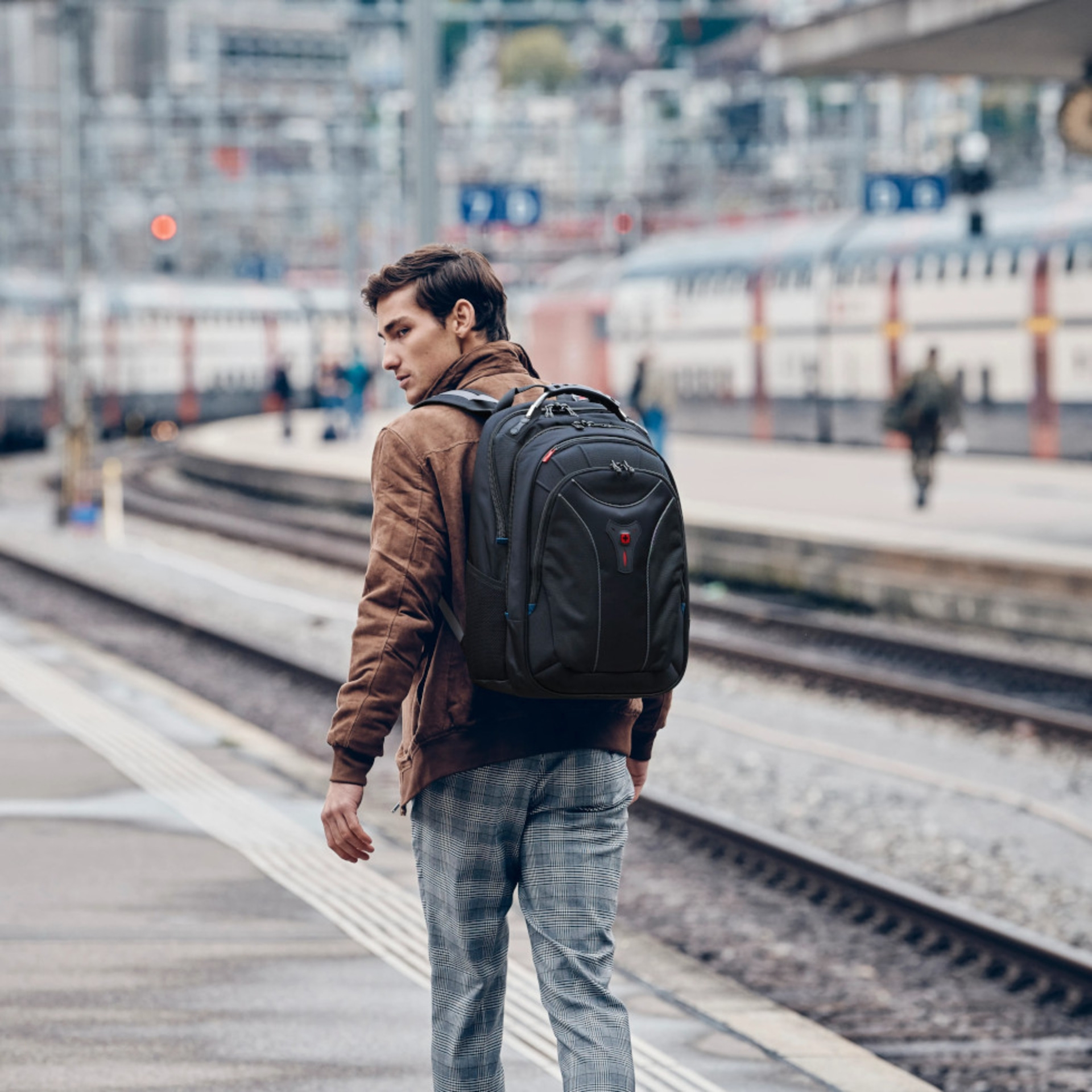 Mann mit Rucksack am Bahnhof, Blick zurück, braune Jacke, karierte Hose, Zug