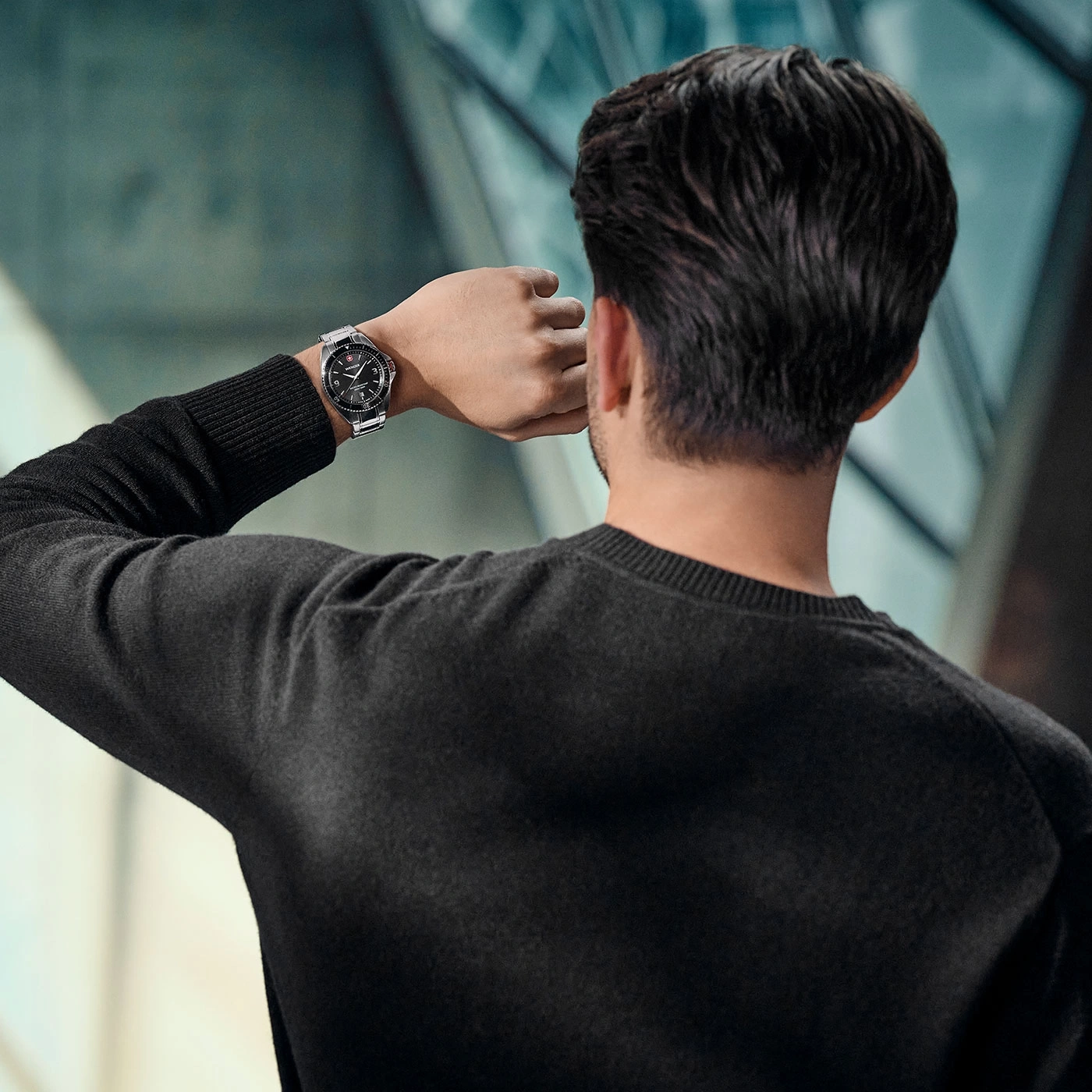 Man looking at his watch, wearing a black sweater, with a blurred background