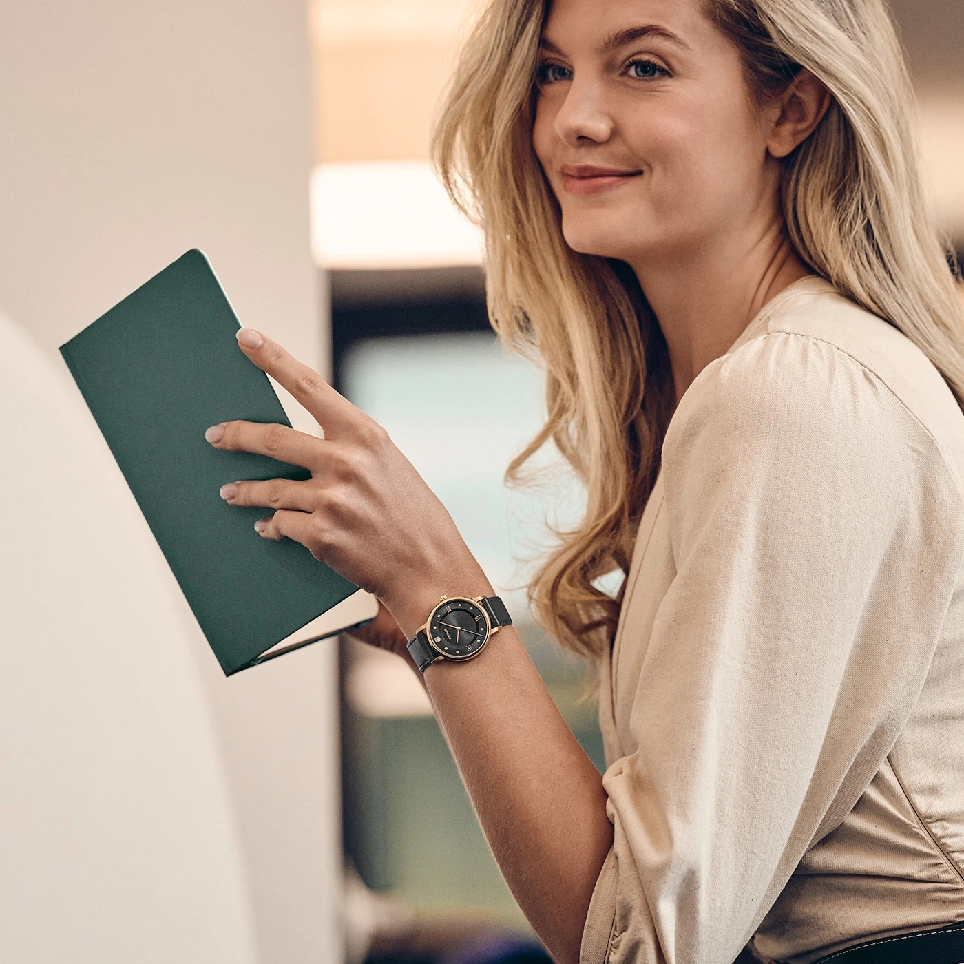A blonde woman holds a green book in her hands.
