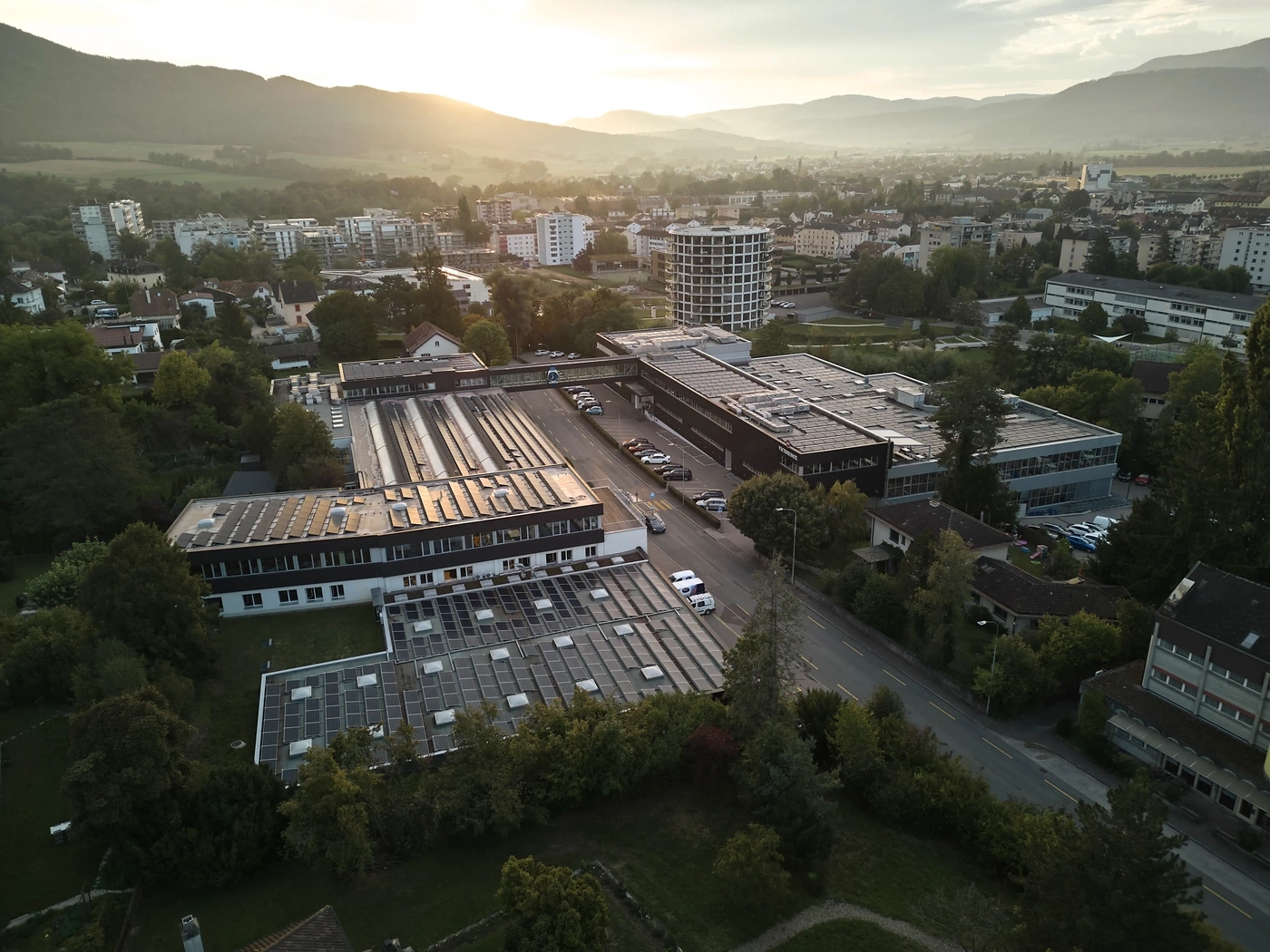 Vue aérienne d'une zone industrielle avec panneaux solaires et montagnes à l'horizon au coucher du soleil.
