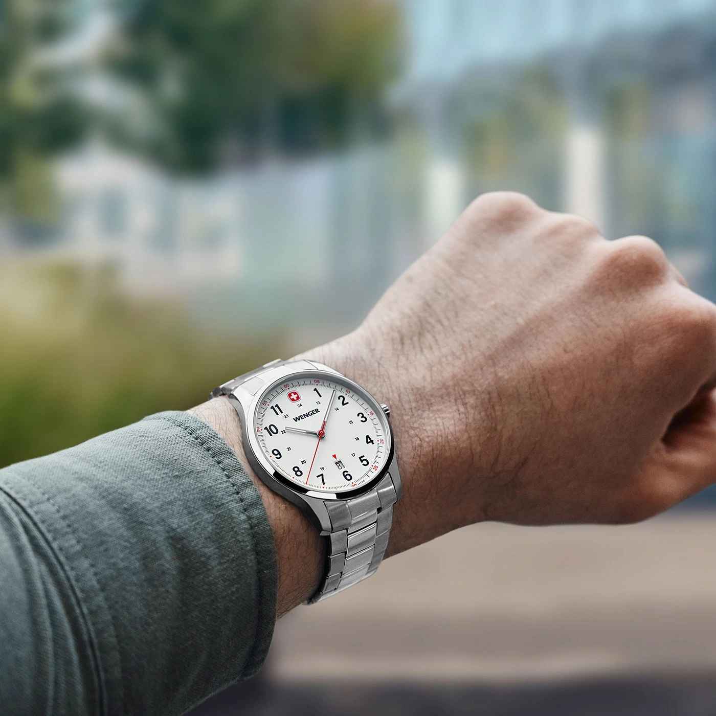 Close-up of a silver Wenger watch on a person's wrist, wearing a green shirt.