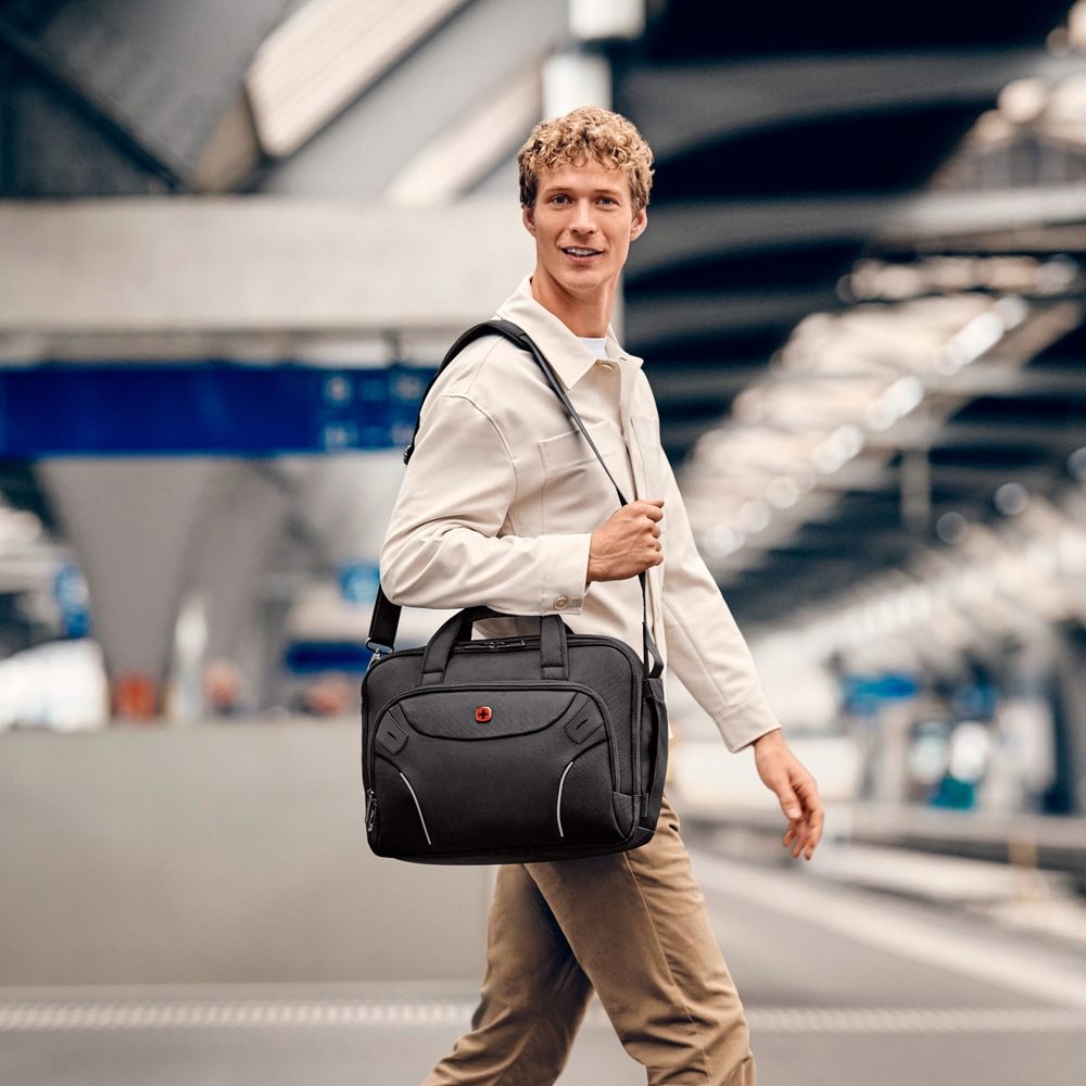 Mann mit schwarzer Tasche geht an einem Bahnhof vorbei und lächelt.