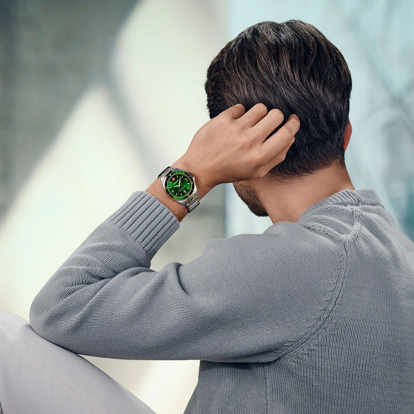 Mann mit Uhr, der sich am Kopf kratzt, grauer Pullover, helle Hose