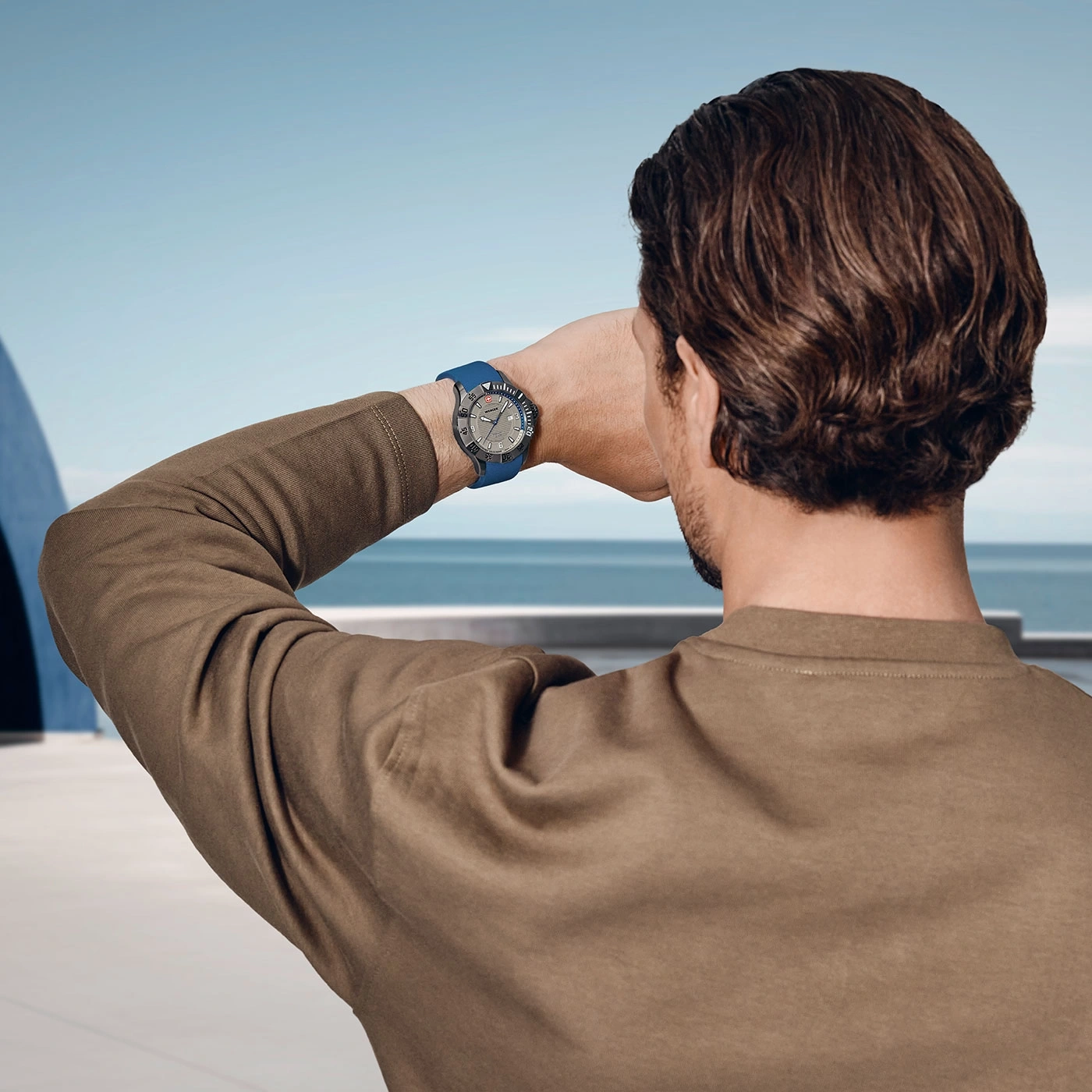 Mann mit Uhr, der auf das Meer blickt, braunes Hemd, blauer Hintergrund