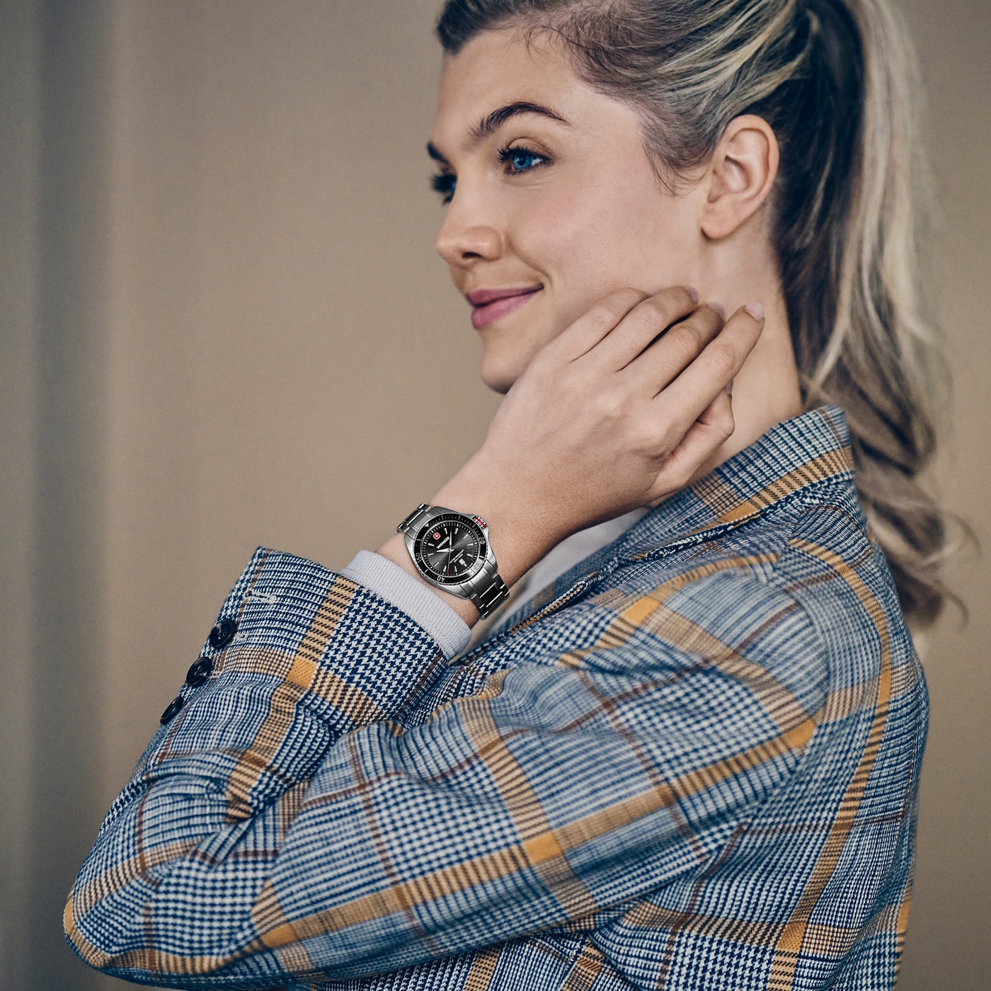 A woman with blue eyes wears a checkered blazer and a watch on her wrist.