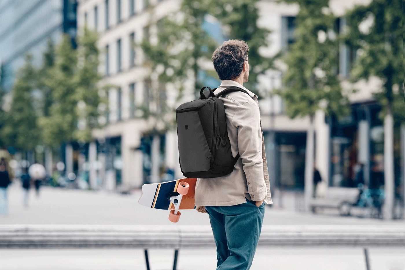 Mann mit Rucksack und Skateboard steht auf der Straße.