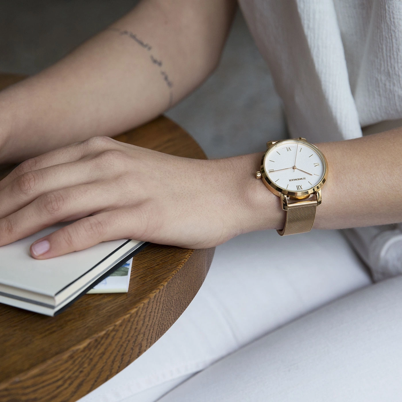 Nahaufnahme einer Person mit goldener Uhr und Notizbuch auf einem Holztisch