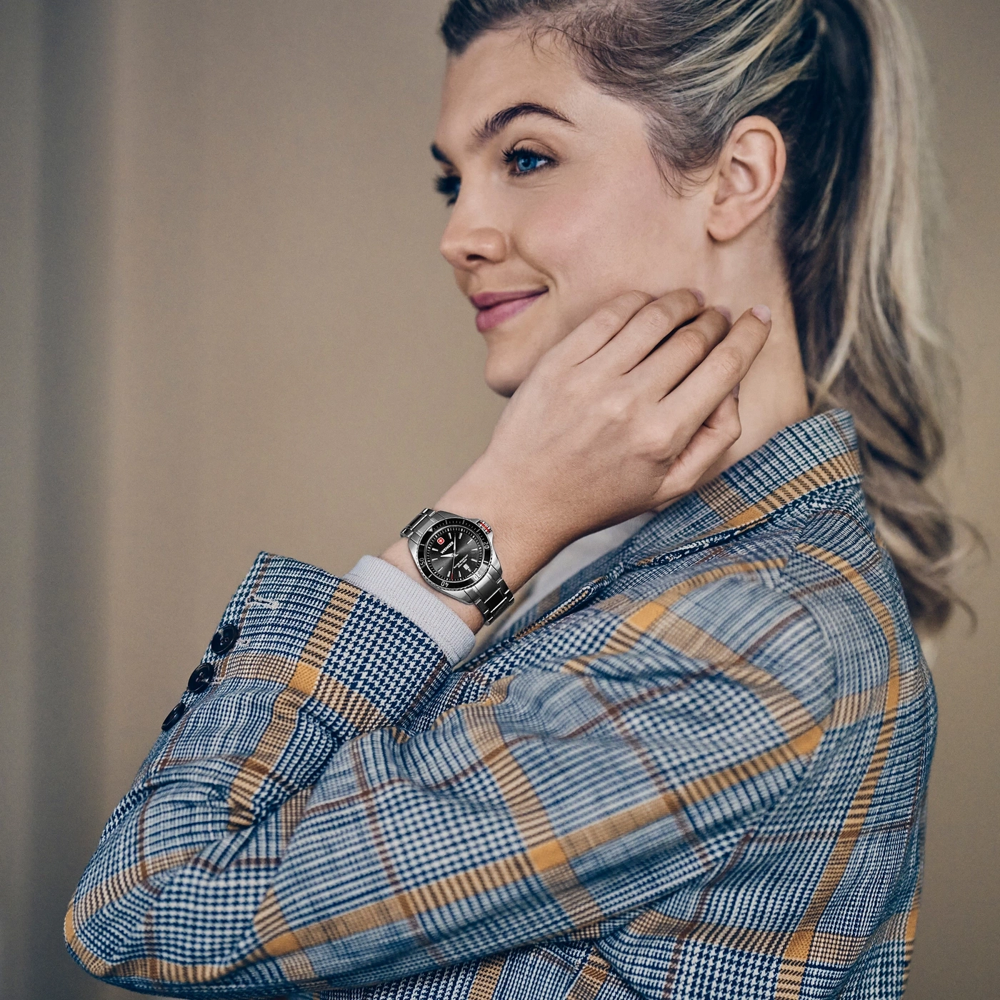 Eine Frau mit blauem Blick trägt einen karierten Blazer und eine Uhr am Handgelenk.