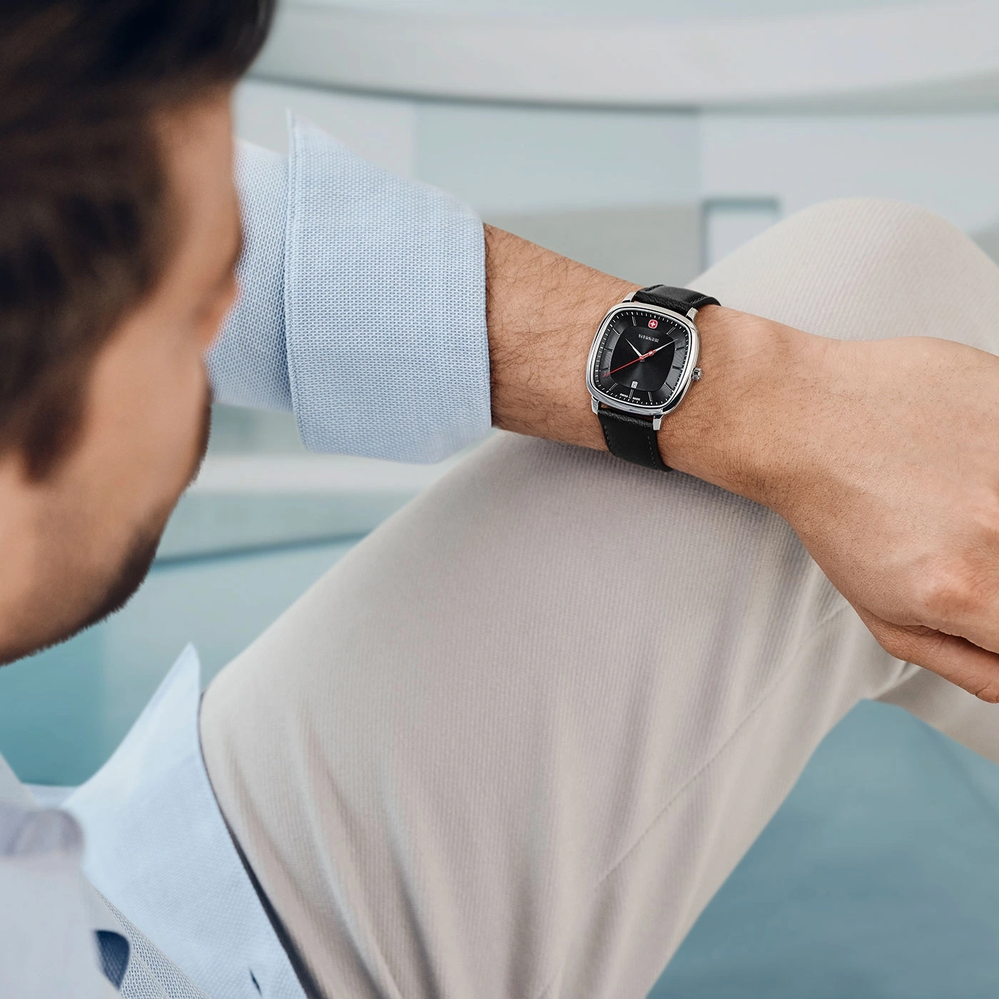 Man wearing watch, black leather strap, light blue shirt, beige pants, wrist