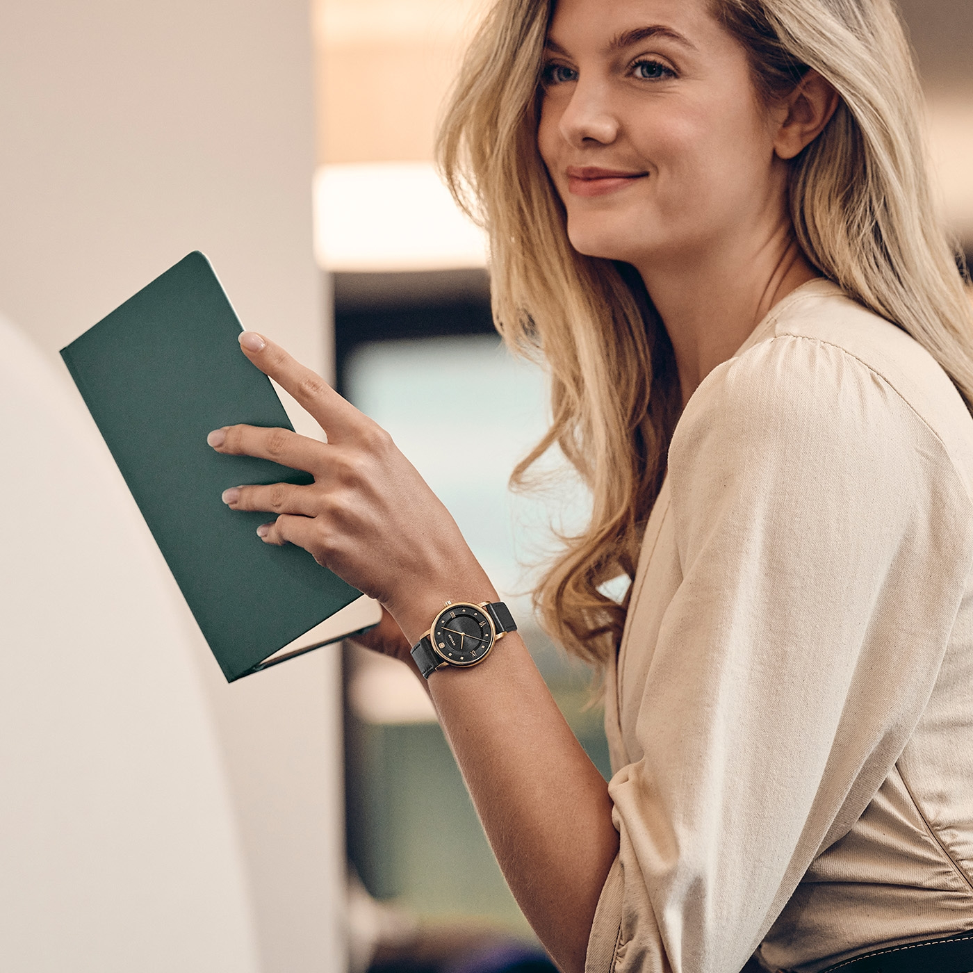 Eine Frau mit blonden Haaren hält ein grünes Buch in der Hand.