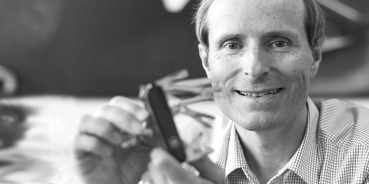 A man holds a multitool in front of his face and smiles.