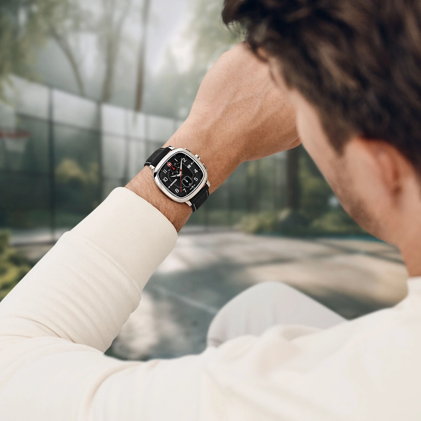 Man wearing watch outdoors with blurred background, looking at his wrist.