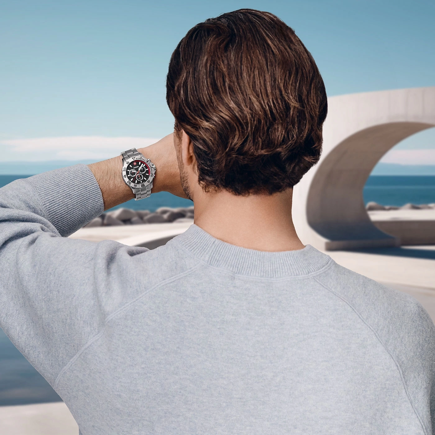 Man with watch looking at the sea in front of a modern building, back view.
