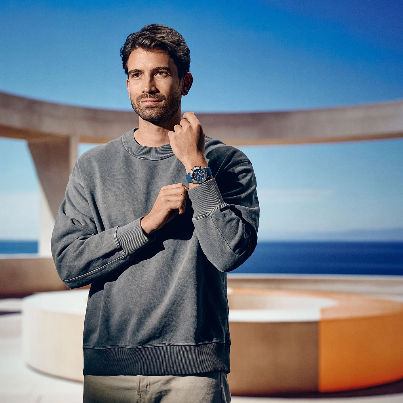 Mann mit Uhr, grauer Pullover, Pose, Hintergrund Meer und Himmel, sonnig