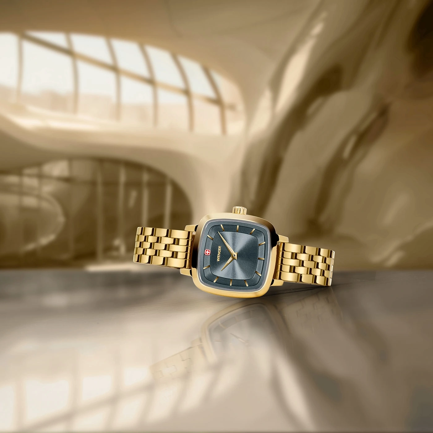 Goldene Uhr mit quadratischem Zifferblatt auf glänzendem Untergrund, Wenger.