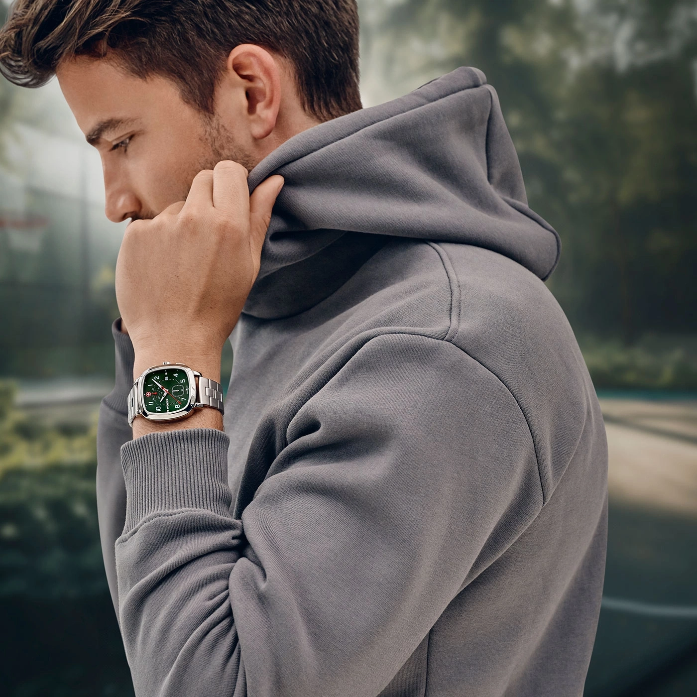 Man wearing watch and hoodie, pulling up the hood, looking down.