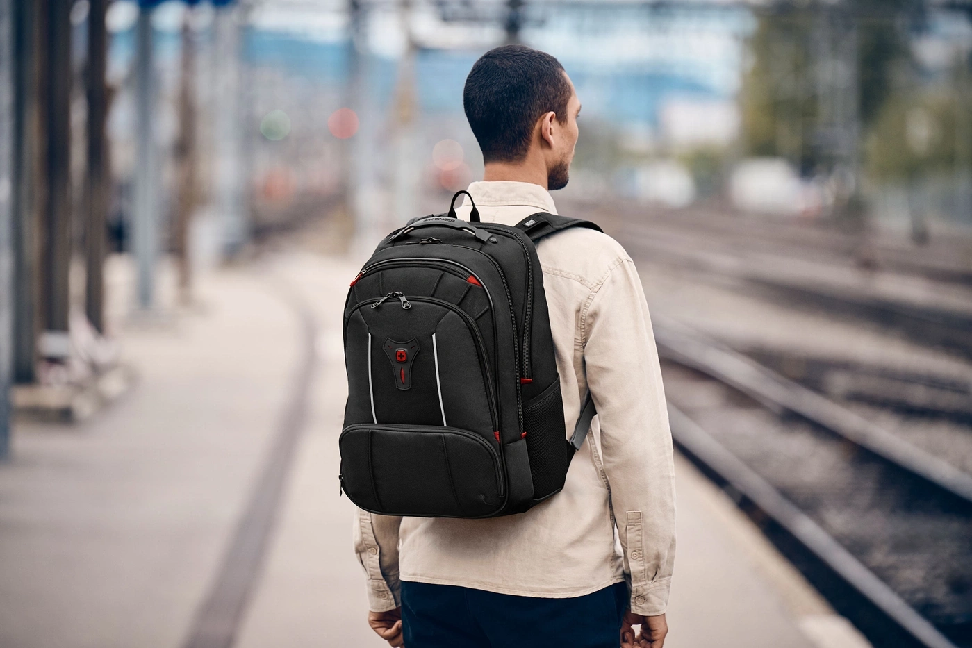Homme avec sac à dos sur le quai de la gare, regardant les voies.