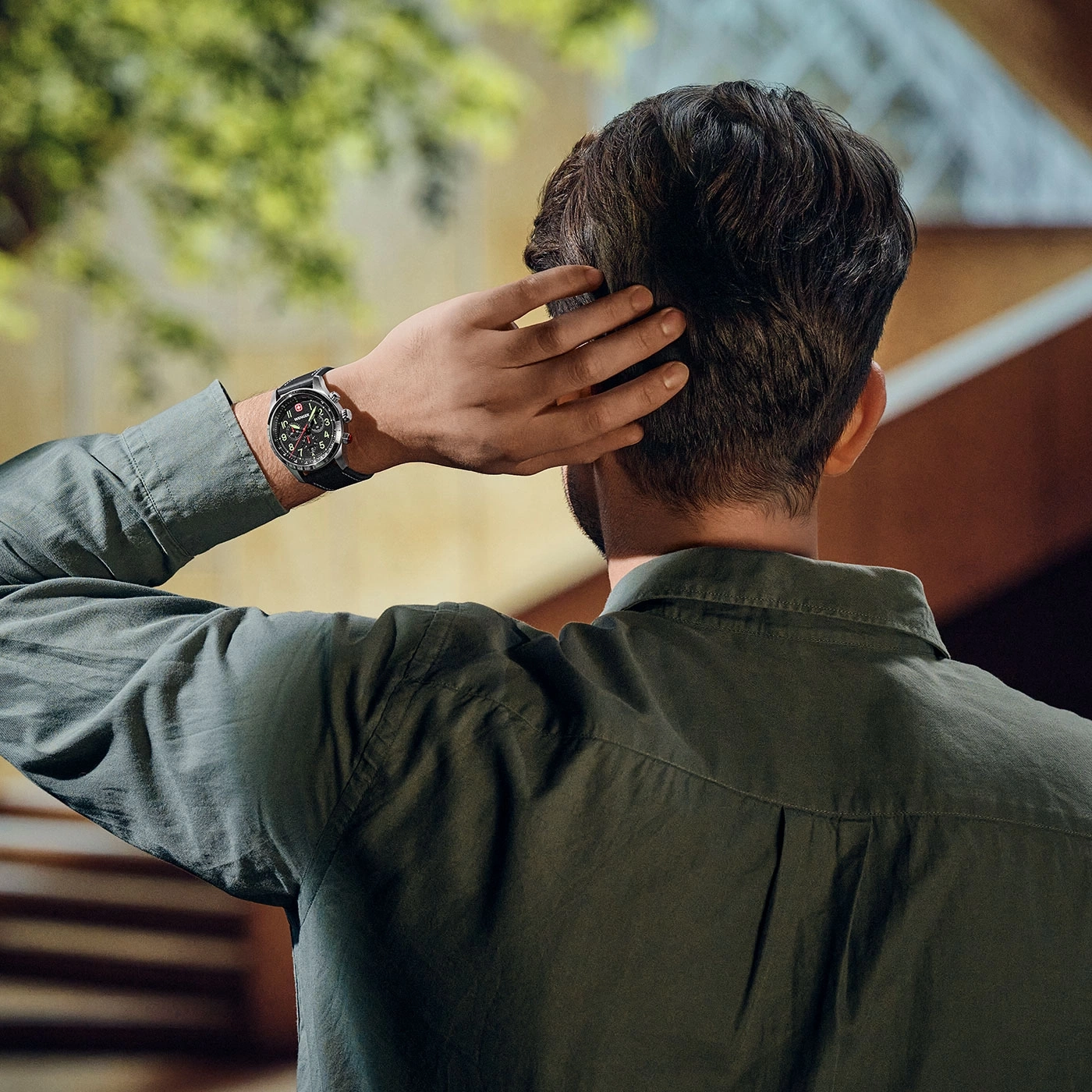 Mann mit Uhr, der sich am Hinterkopf kratzt, in einem grünen Hemd.