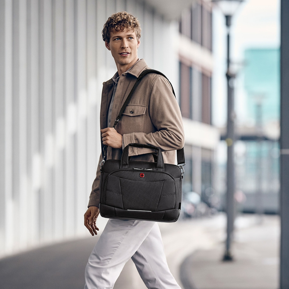 Mann mit schwarzer Tasche, der vor einem Gebäude spaziert und in die Ferne blickt.