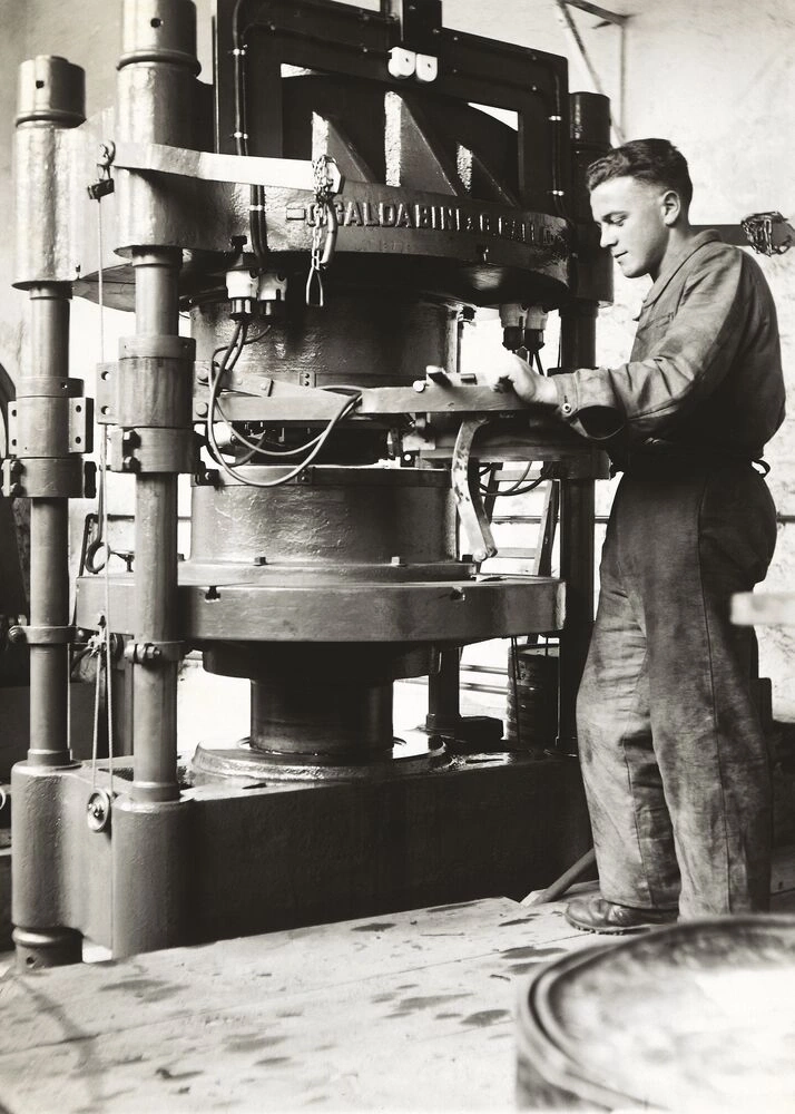 A man operates a large industrial press in a workshop setting.