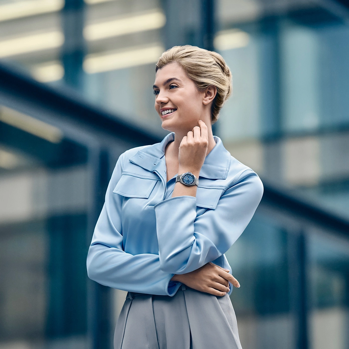 Frau in hellblauer Bluse und grauem Rock, die auf eine Uhr blickt.