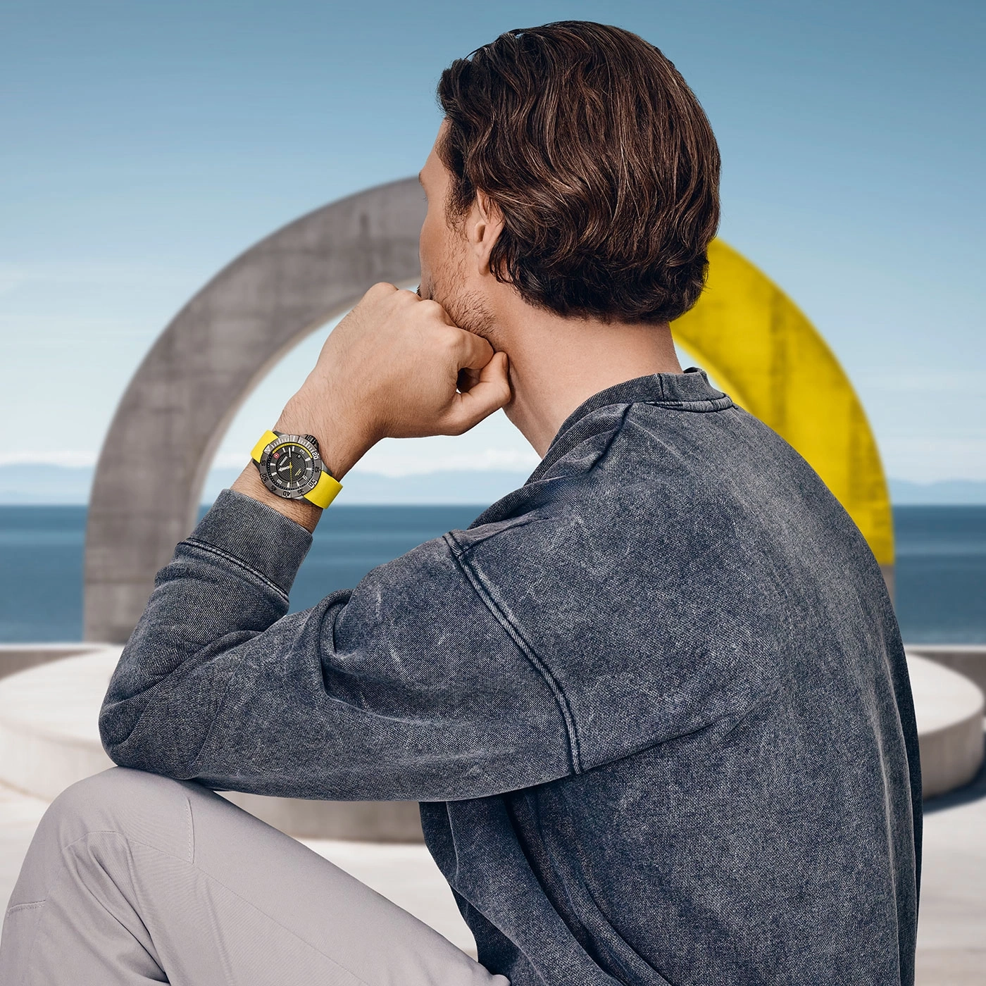 Mann mit Uhr, der auf das Meer blickt, vor einem gelben Bogen