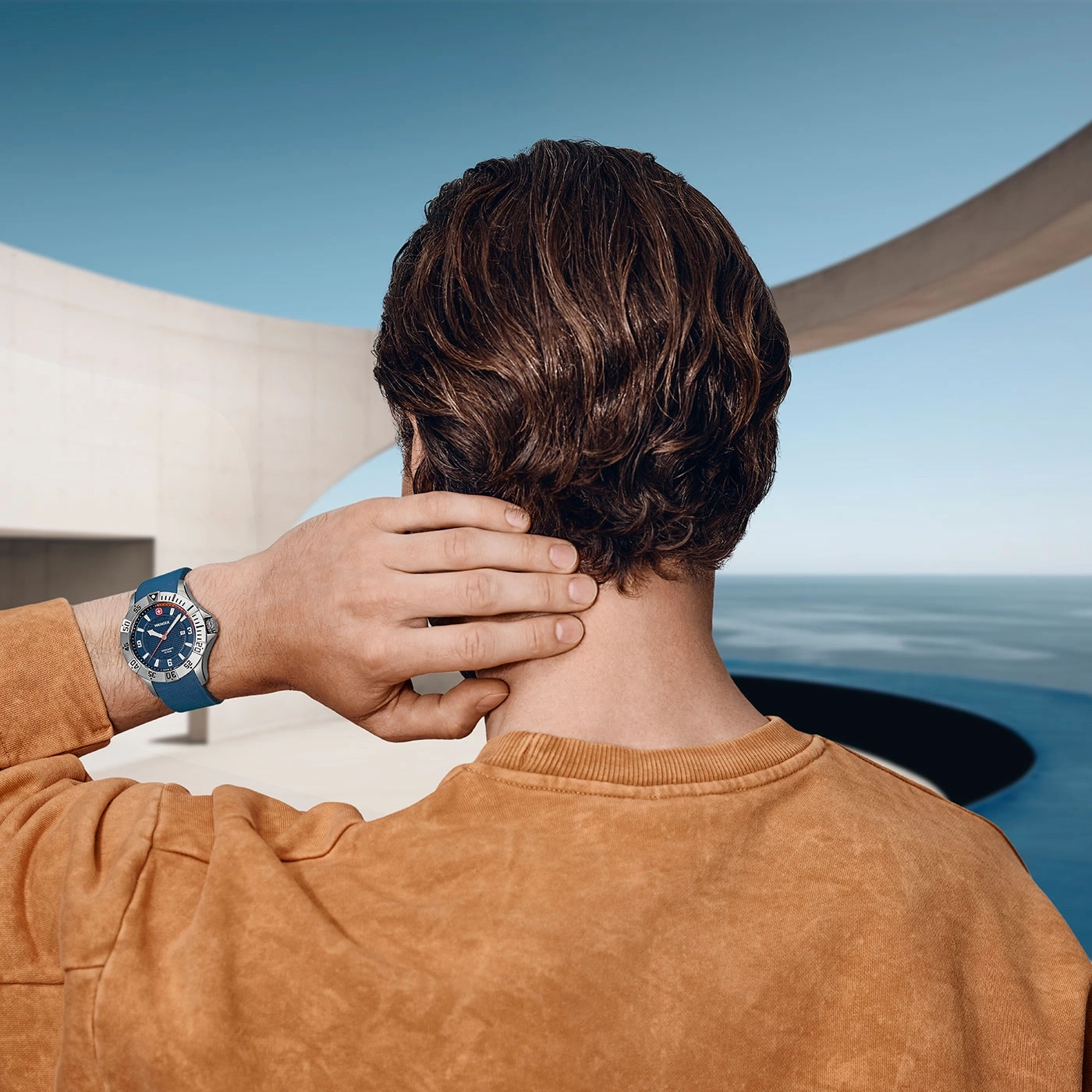 Man with watch scratching neck, in front of sea and building.