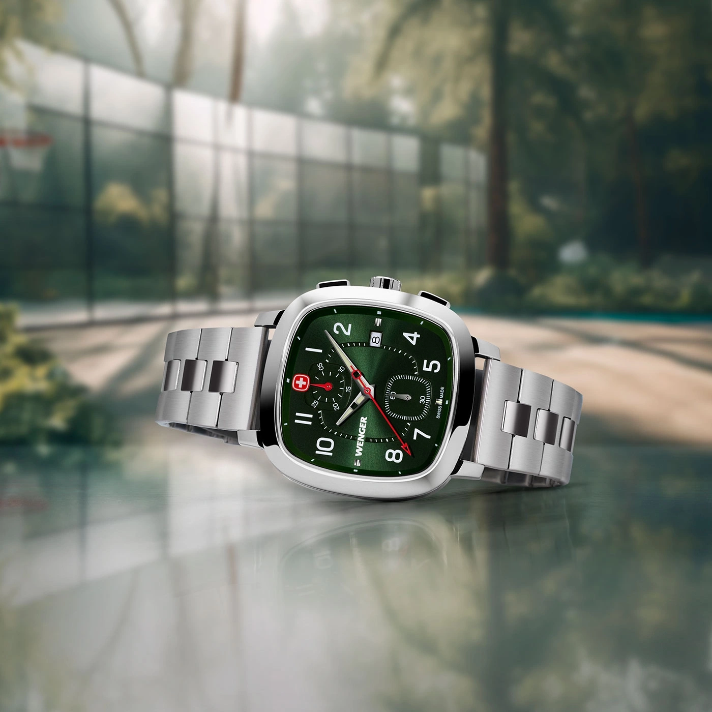 Close-up of a Wenger watch with green face and silver band, set on a reflective surface