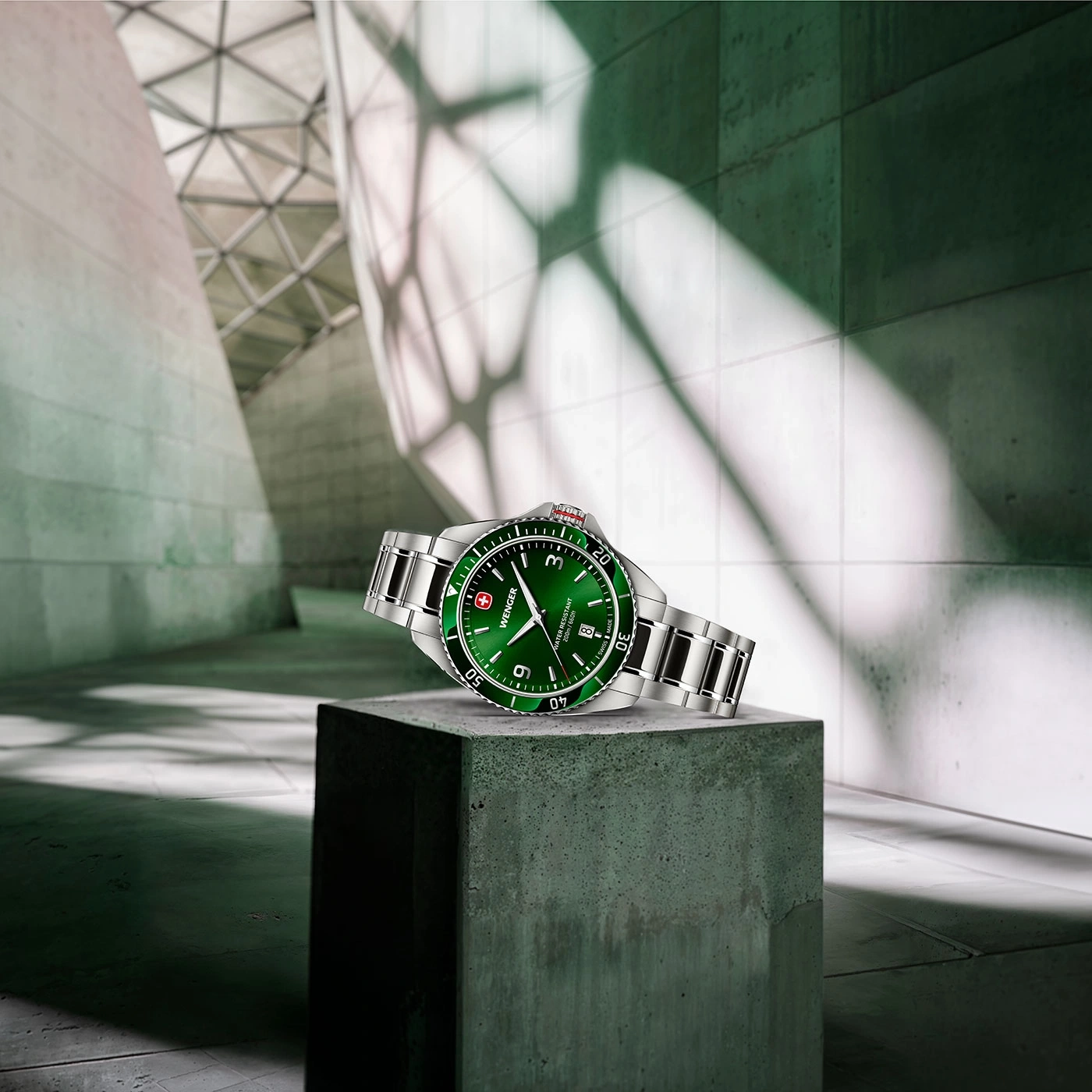 Watch on concrete block, green dial, silver bracelet, modern architecture in background