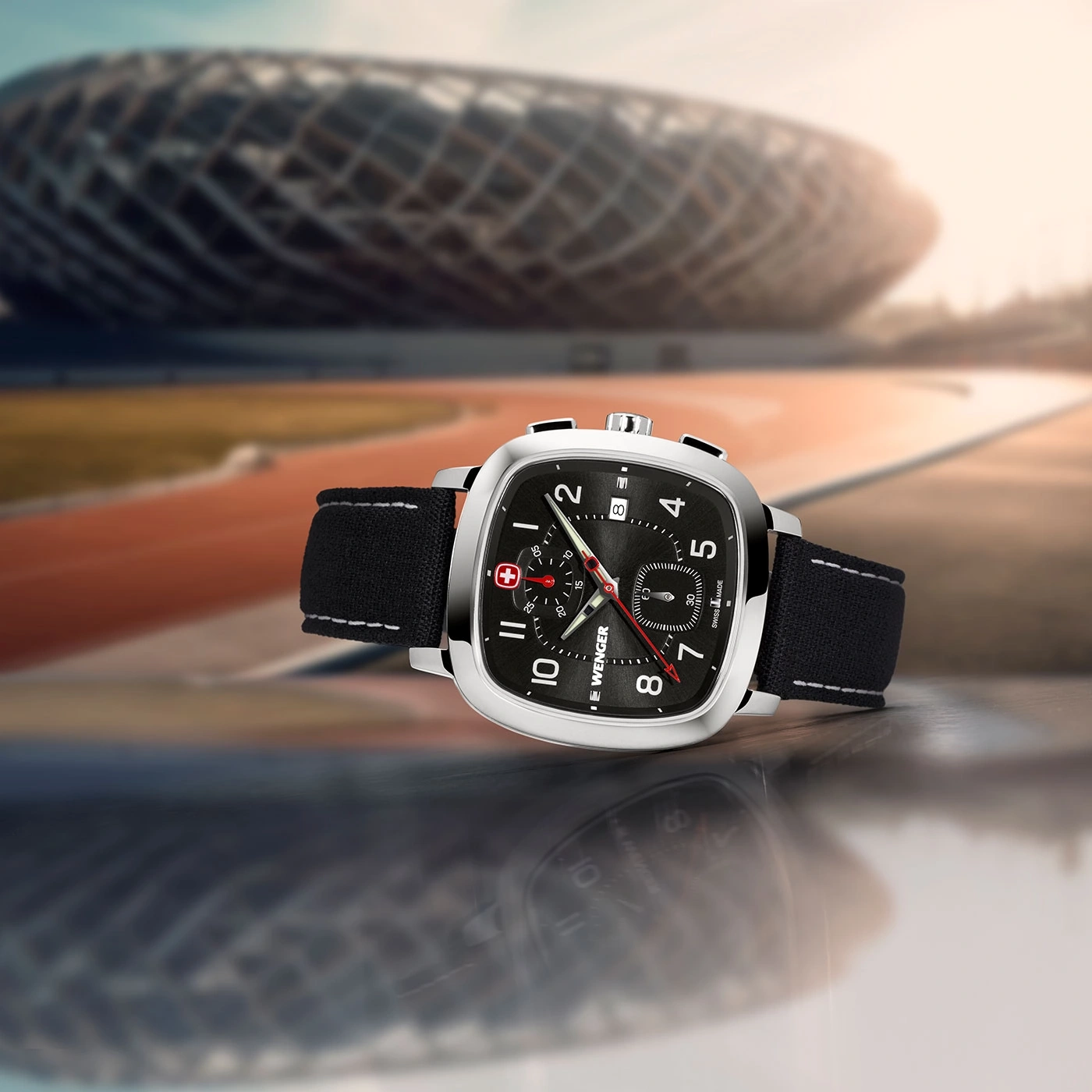 Wenger watch with black face and strap, set against a blurred stadium background.