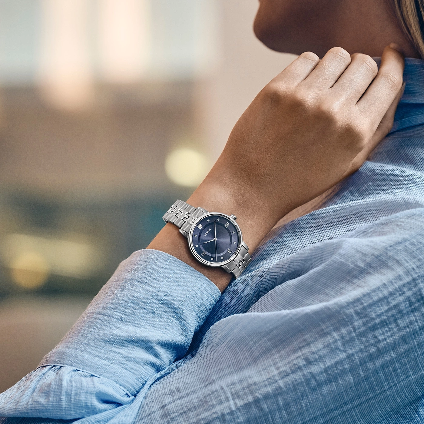Eine Frau mit einer blauen Bluse trägt eine silberne Uhr am Handgelenk.