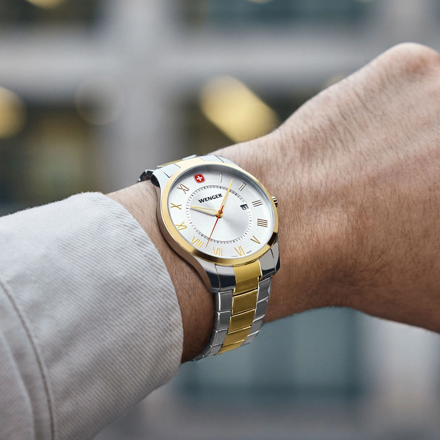 Wenger Uhr am Handgelenk, silber-goldfarbenes Armband, weißes Zifferblatt, römische Ziffern