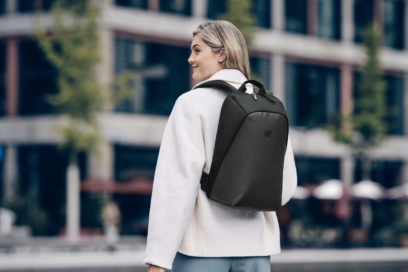 Frau mit schwarzem Rucksack auf dem Rücken, steht vor einem Gebäude.