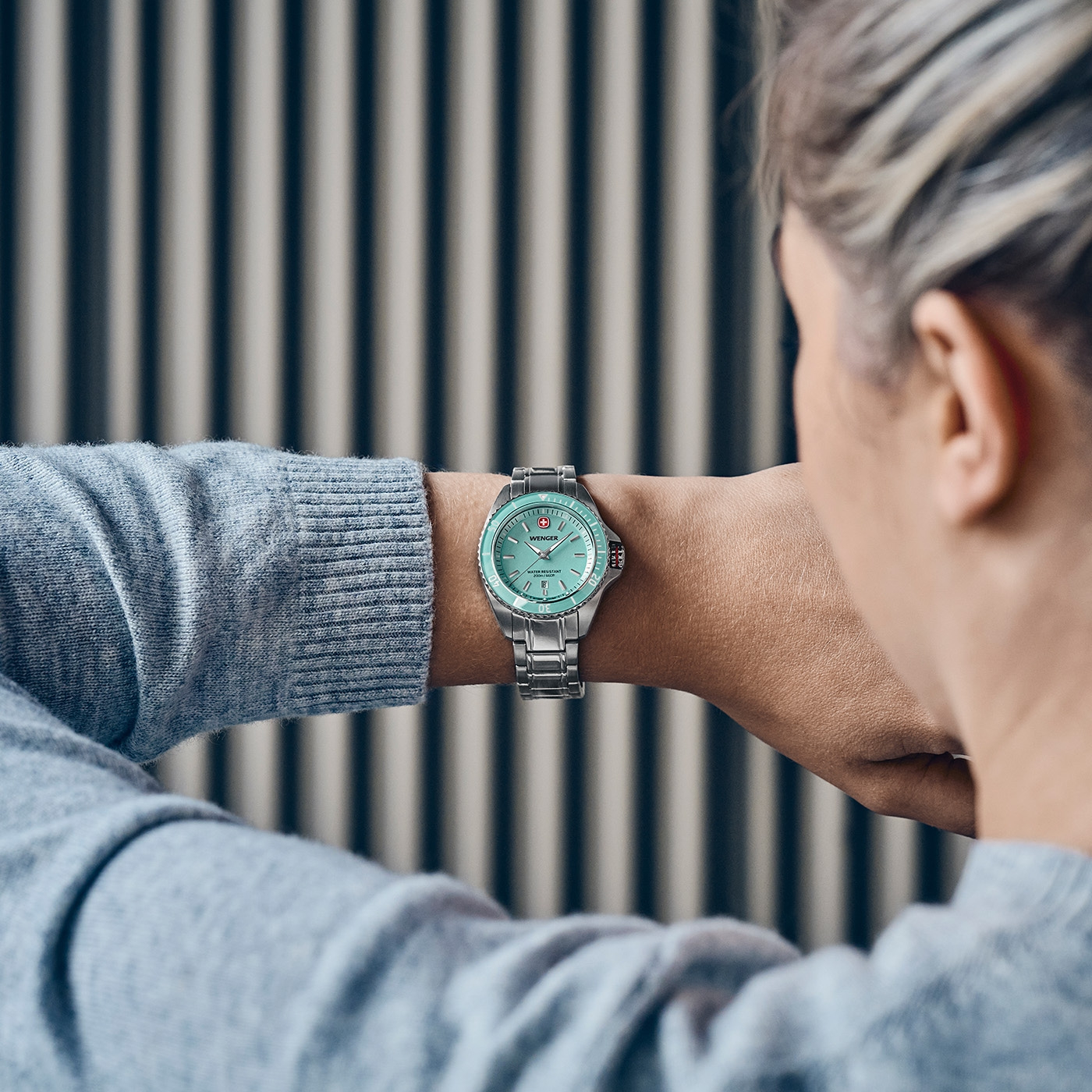 A woman looks at her mint green Wenger wristwatch on her left wrist.