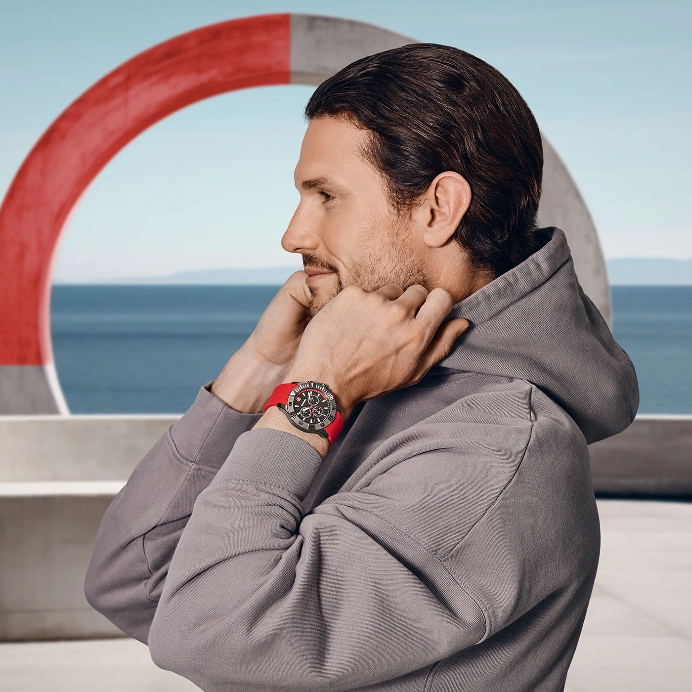 Man with watch and red strap, in front of a red ring, sea in the background