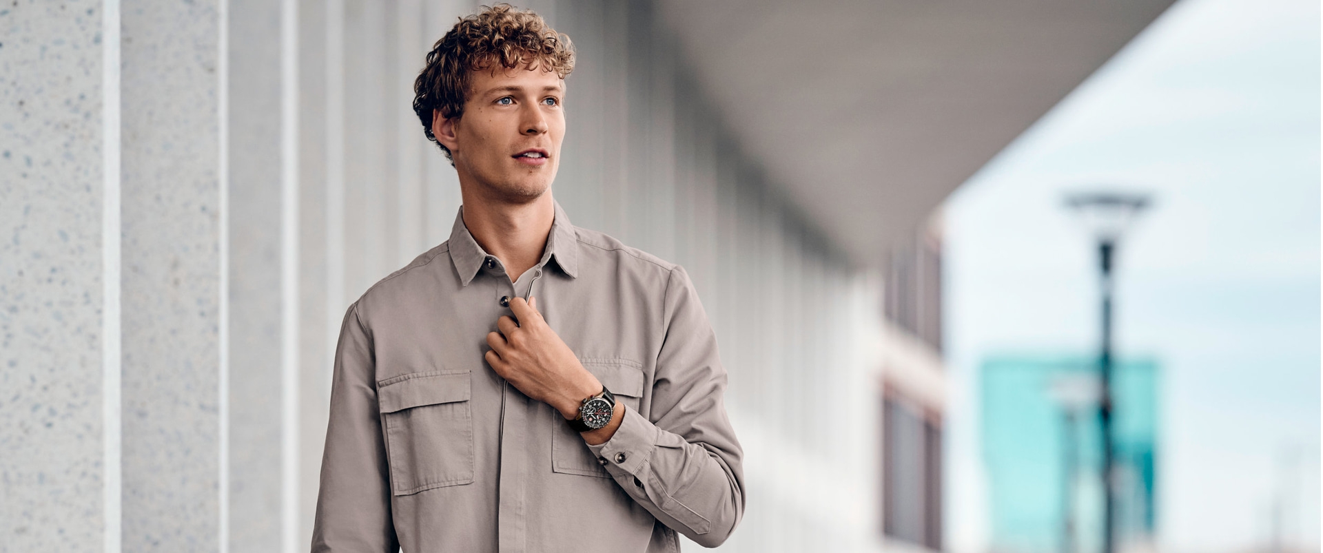 Ein Mann in einem Hemd, der eine Uhr trägt, die an einem Gebäude steht.