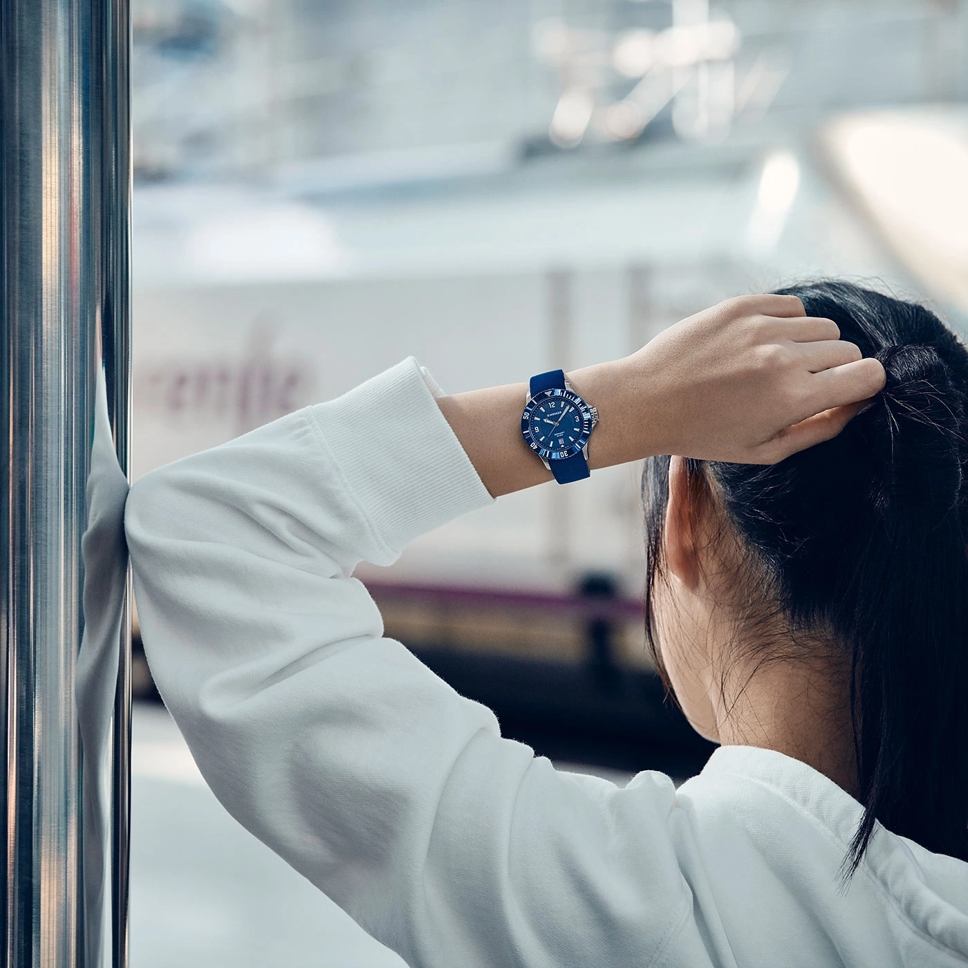 Frau mit Uhr, die aus dem Fenster schaut, in einem weißen Hoodie.